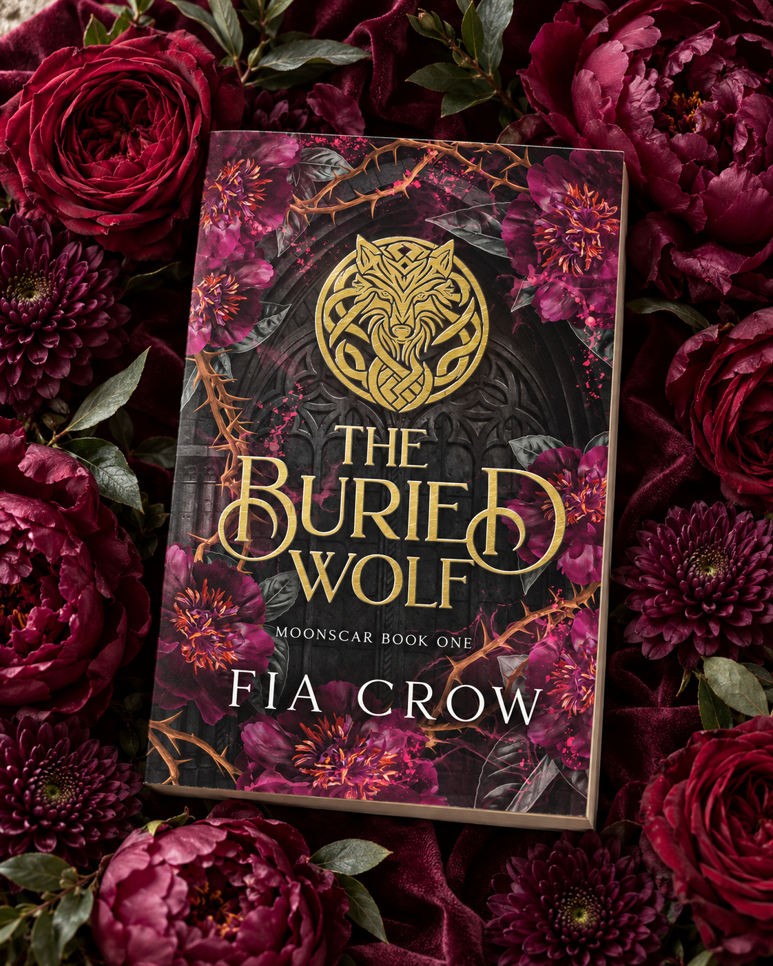 The Buried Wolf paperback surrounded by burgundy roses and peonies on velvet